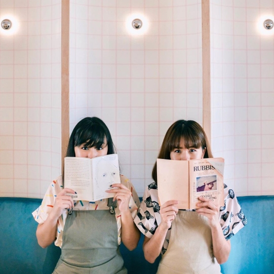 Women holding books against a tiled wall in Looksee Looksee